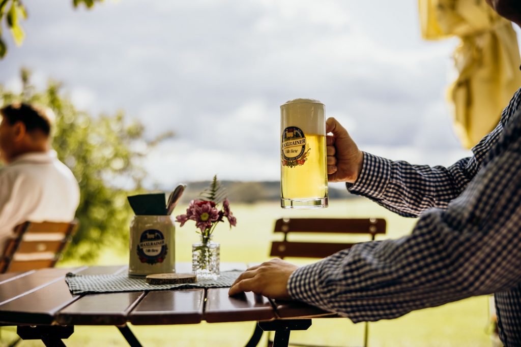 Ein Gast genießt sein Bier (Maxlrainer) im Biergarten mit Panorama Ausblick auf die Berge im Landgut Kugleralm in Ebersberg nahe München